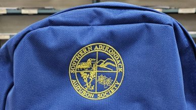 A photo of a blue backpack with a gold logo that says Southern Adirondack Audubon Society.